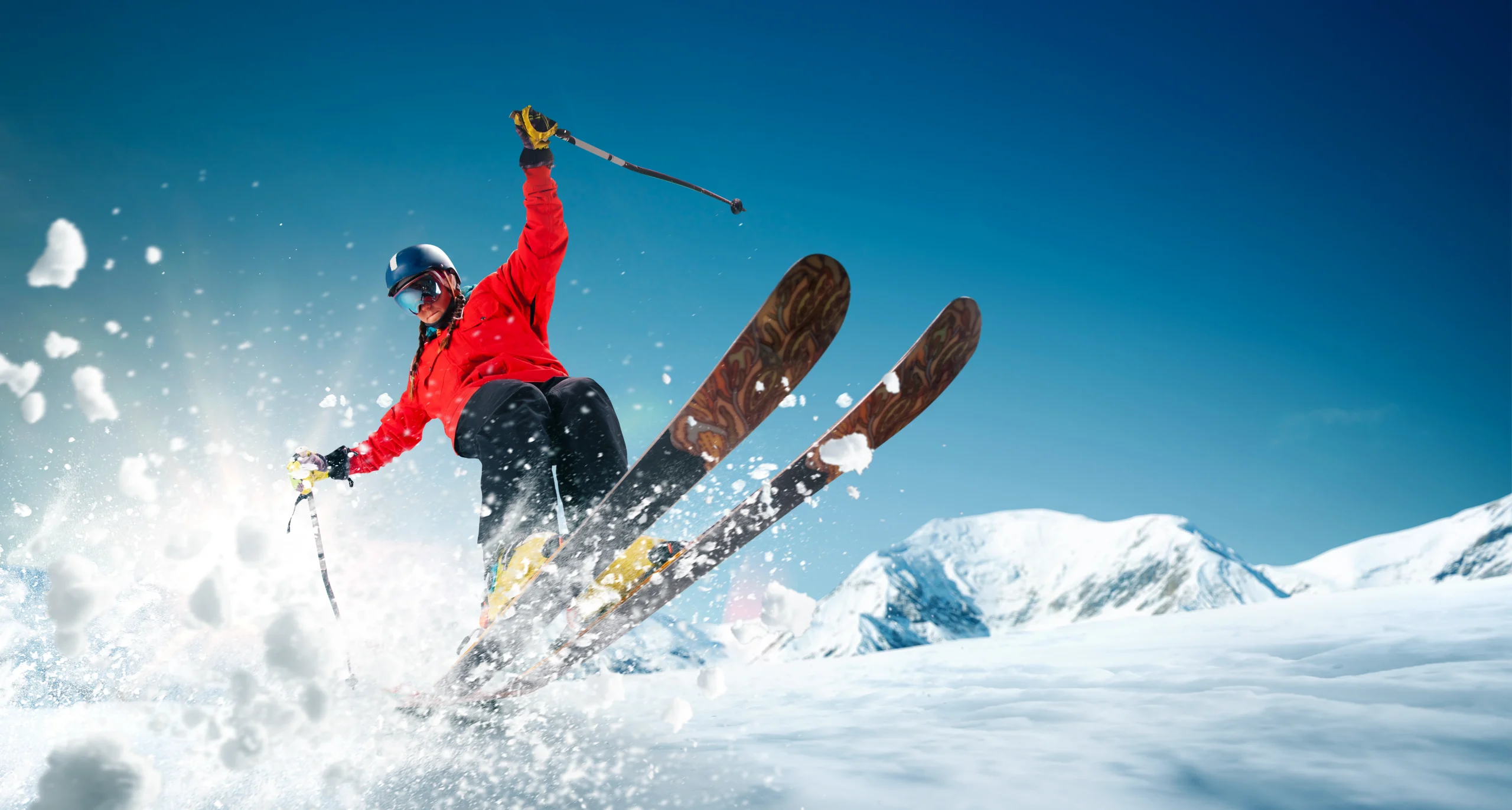 Woman with blonde braids and a red jacket skiing and kicking up snow into the camera frame