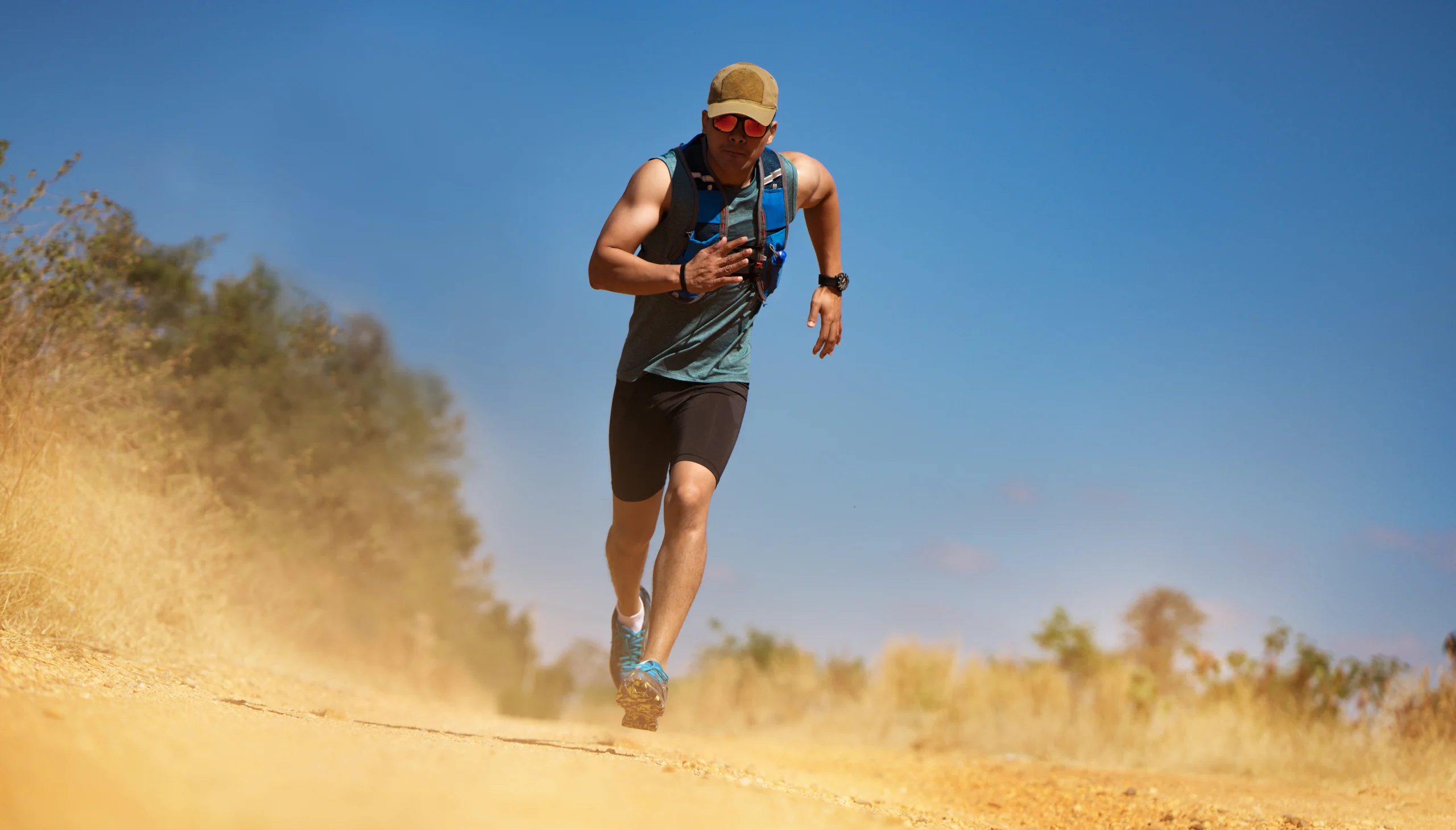 Man with a yellow hat and sunglasses running on a desert trail